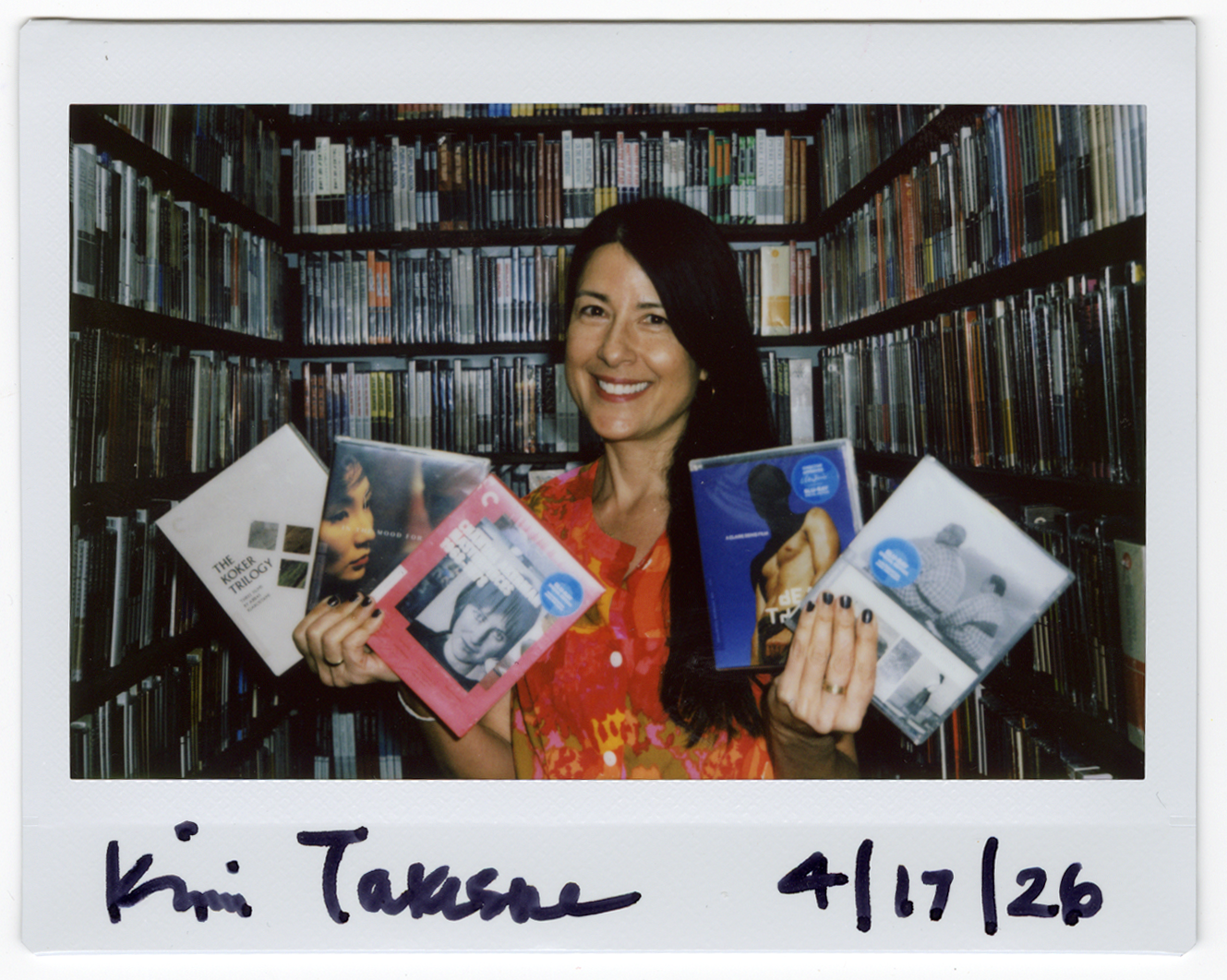 Kimi Takesue inside the Criterion Closet. A scanned Instax of Kimi. She holds Blu-rays and DVDs in her hands and smiles at the camera.