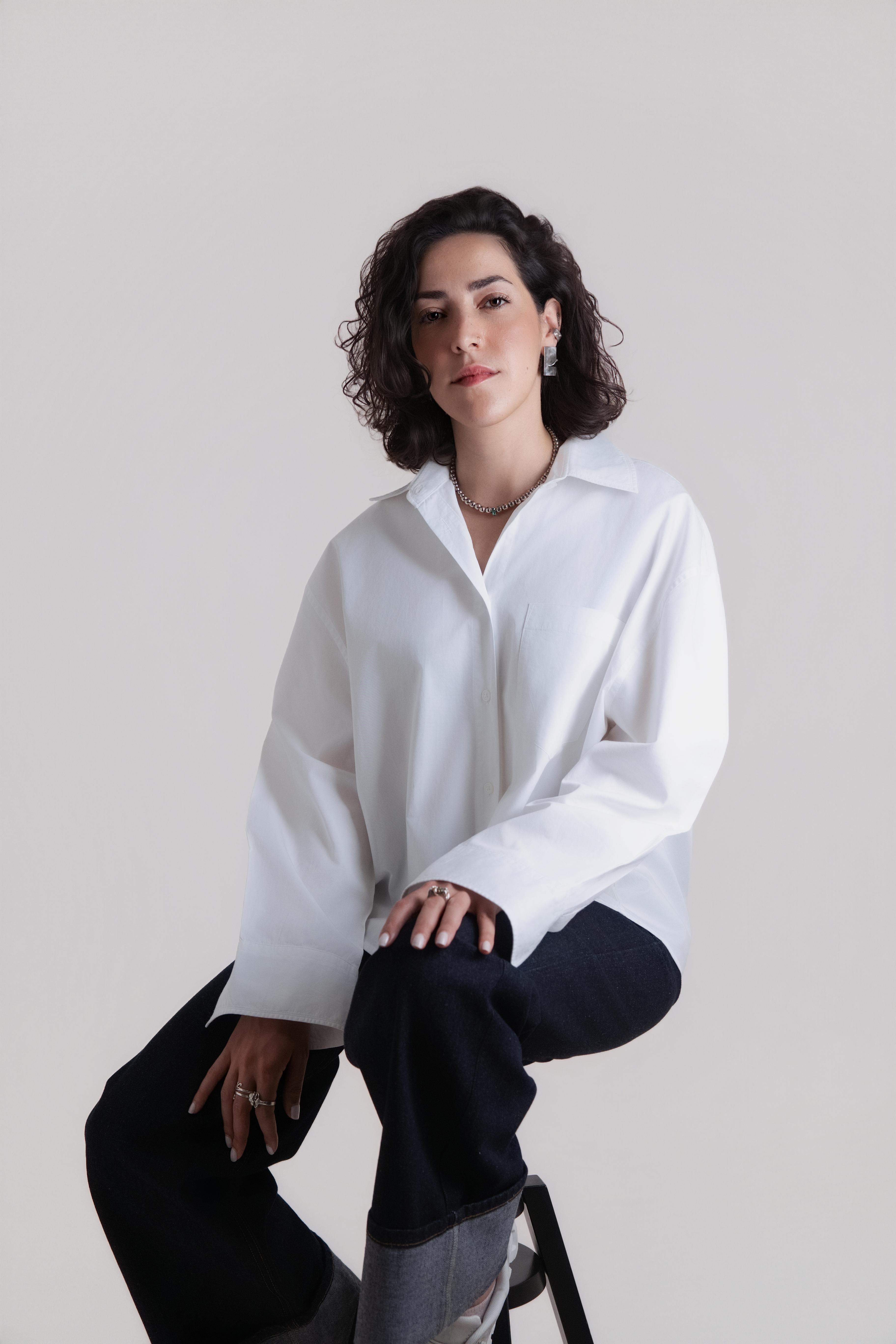 Brown/black curly-haired woman in a white shirt in a studio with a white backdrop