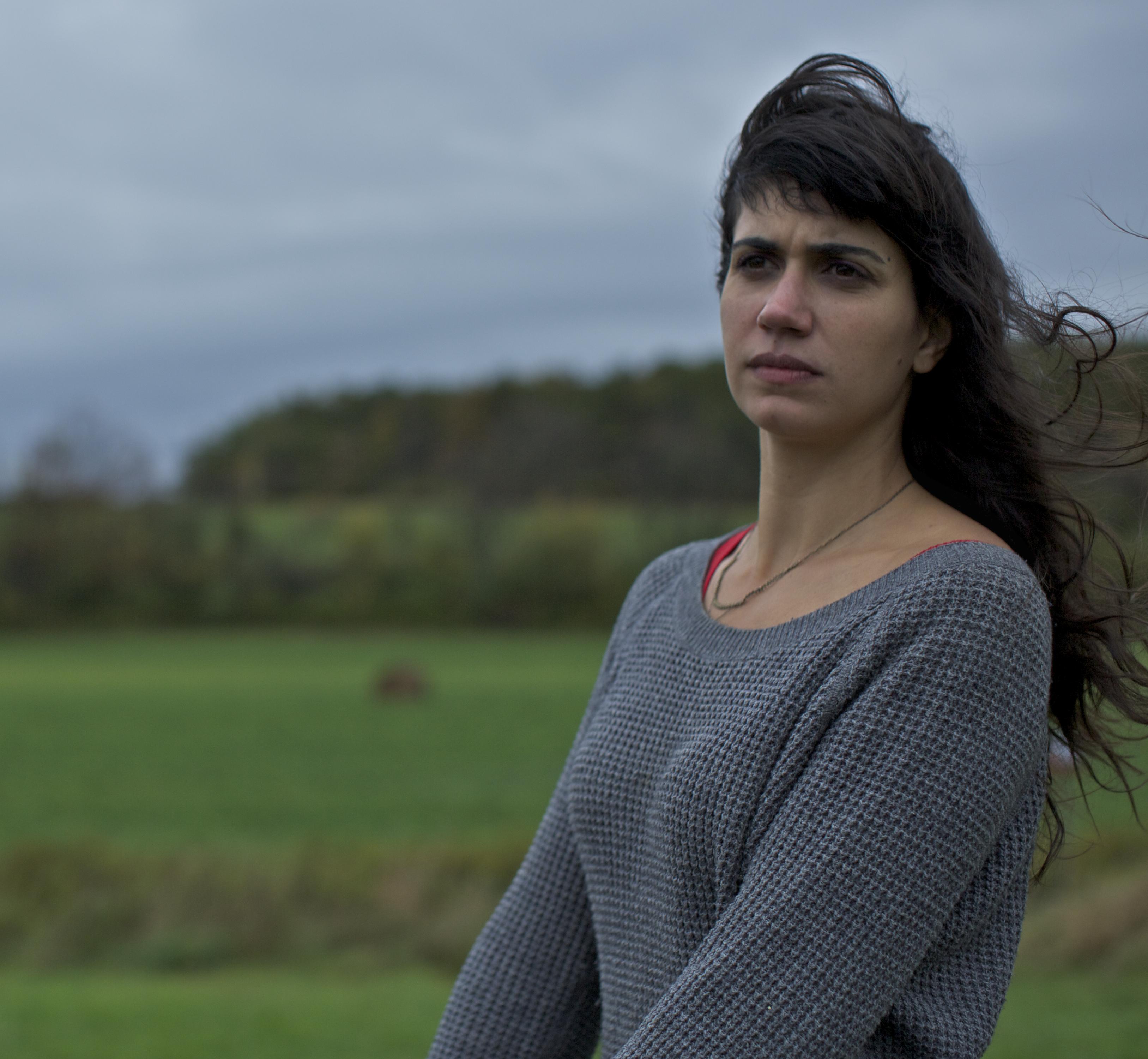 Jessica Dimmock looks away from the camera. She is outside and her brown hair is flowing in the wind.
