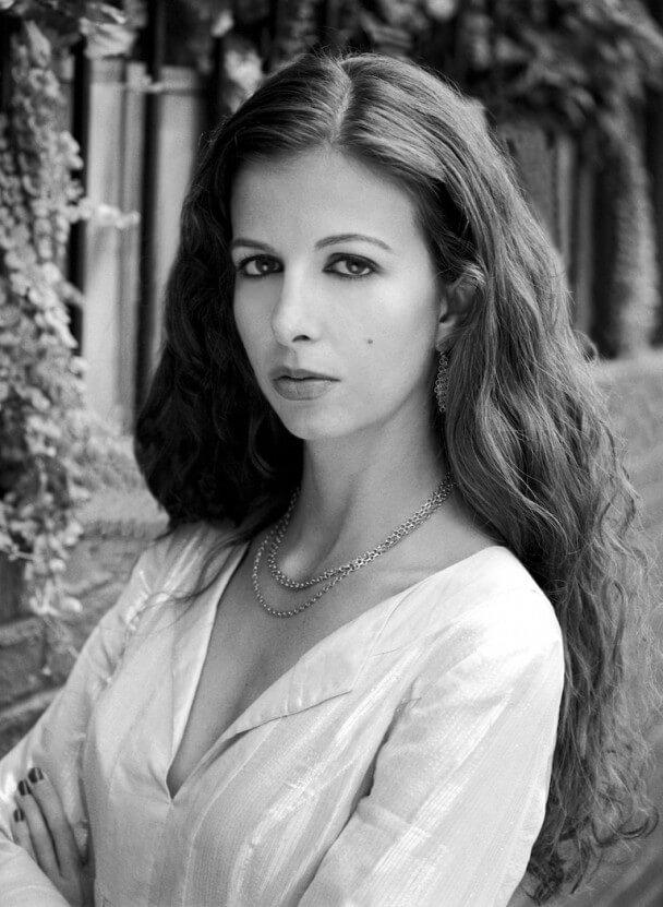 A black and white photo of a woman with her arms crossed looking into the camera.