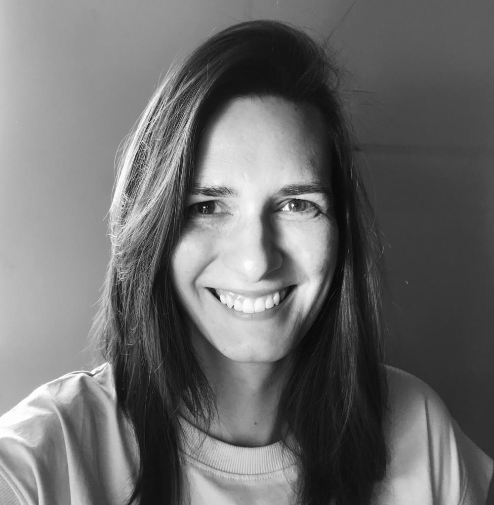 Kasia Kuczyńska looking directly at camera and is smiling. She has long, dark hair and is wearing a crew neck shirt. Black and white portrait.