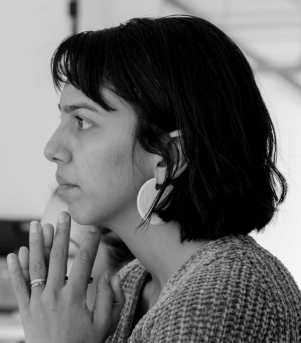 A woman with shoulder-length dark hair and bangs  looks intently to the left with her chin resting lightly on her fingers. Headshot of Natalie Patillo