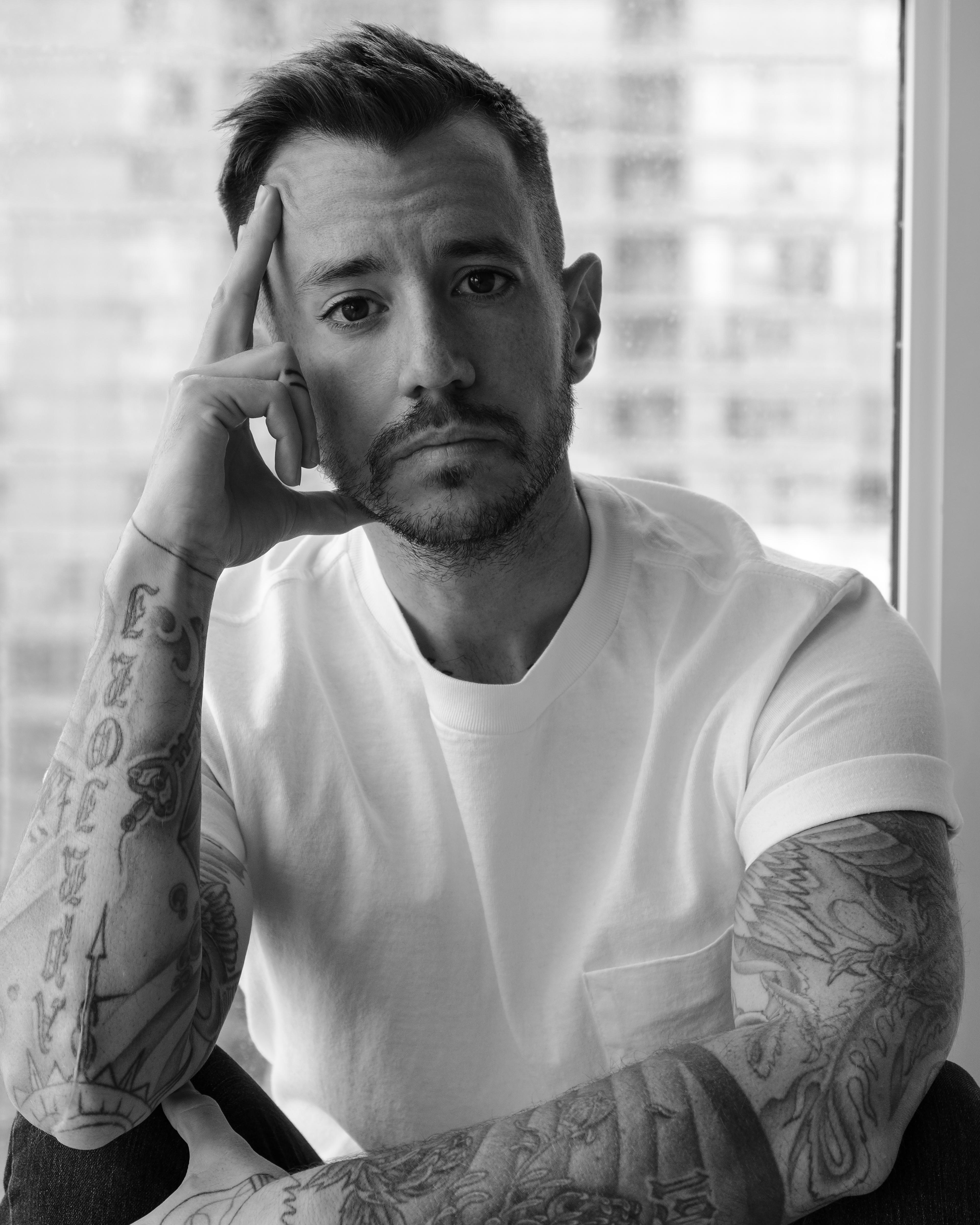 Black and white photo of man with tattoos wearing a white t-shirt.
