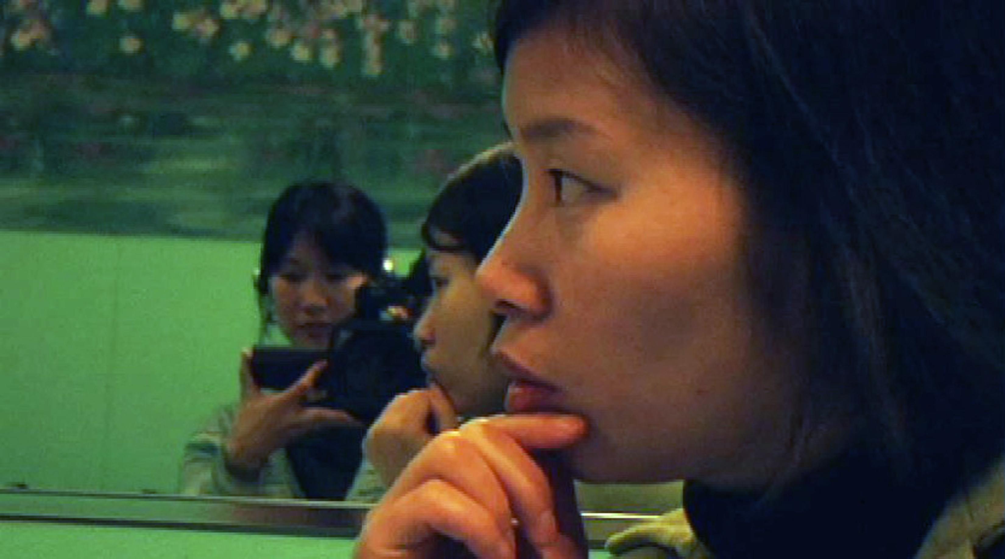Woman with a camera films a woman who looks focused in the mirror.