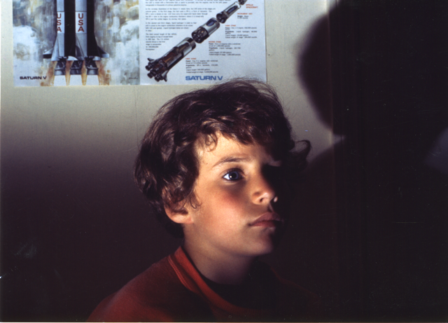Still from Earth Camp One. A young boy looks away from the camera. The light illuminates part of his face and leaves the rest in the shadow.